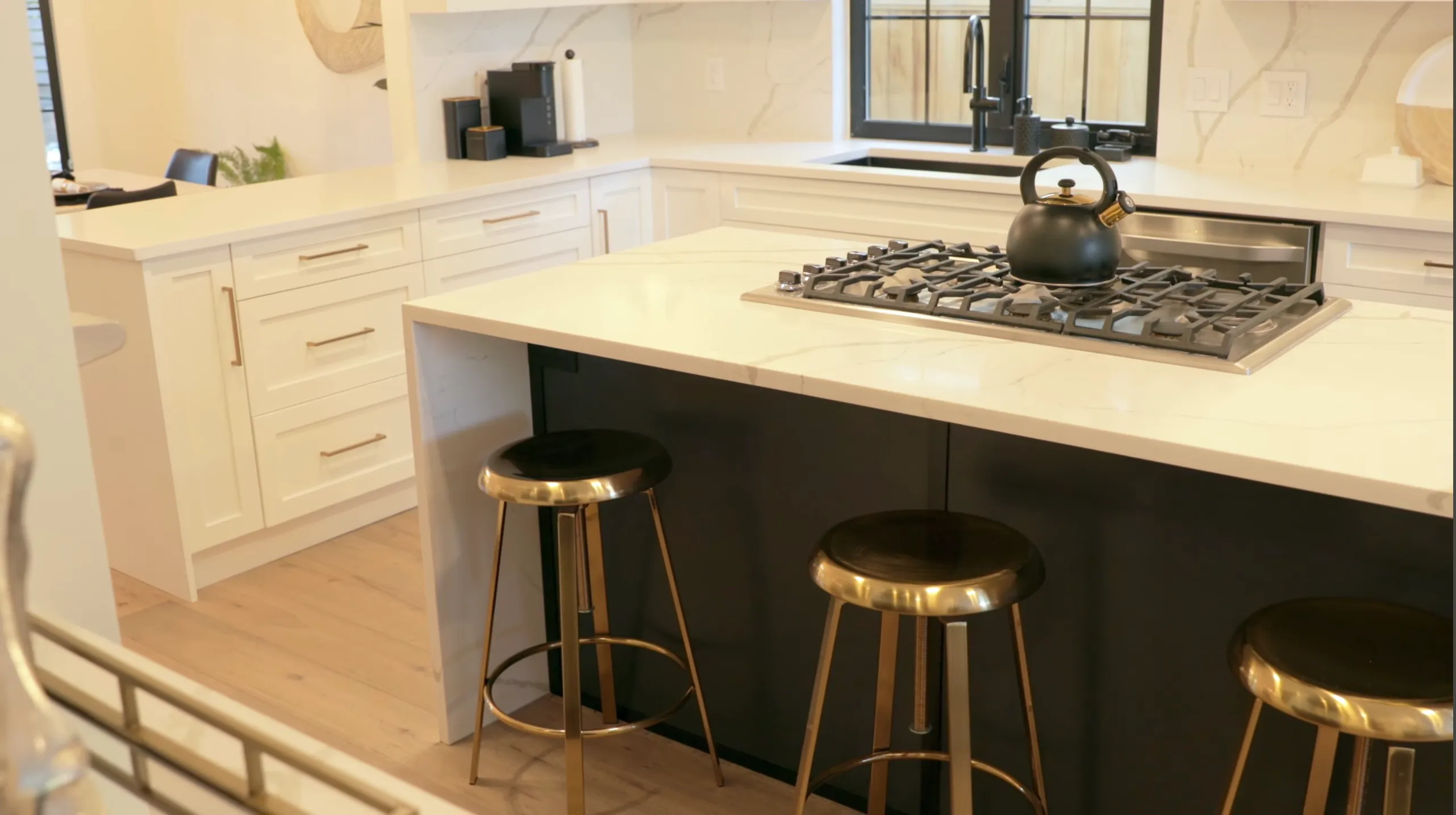 Renovated open-plan kitchen with marble waterfall island, gas cooktop, brass bar stools and two-tone cabinetry — kitchen renovation Vancouver by DELANA Interiors