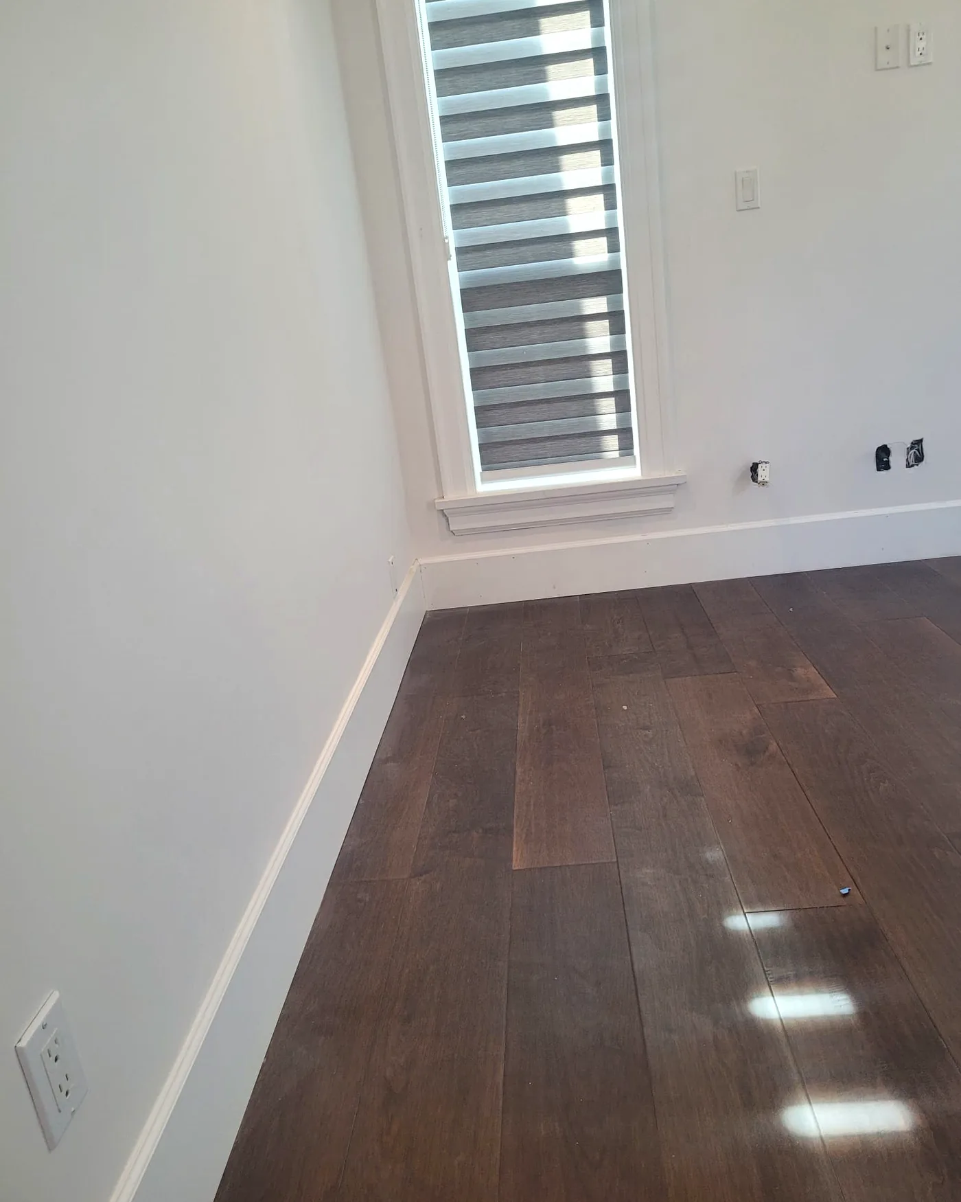 New dark hardwood flooring, custom baseboards and freshly painted trim in a renovated room — full home renovation by DELANA Interiors at 7291 Parry Street, Richmond, BC
