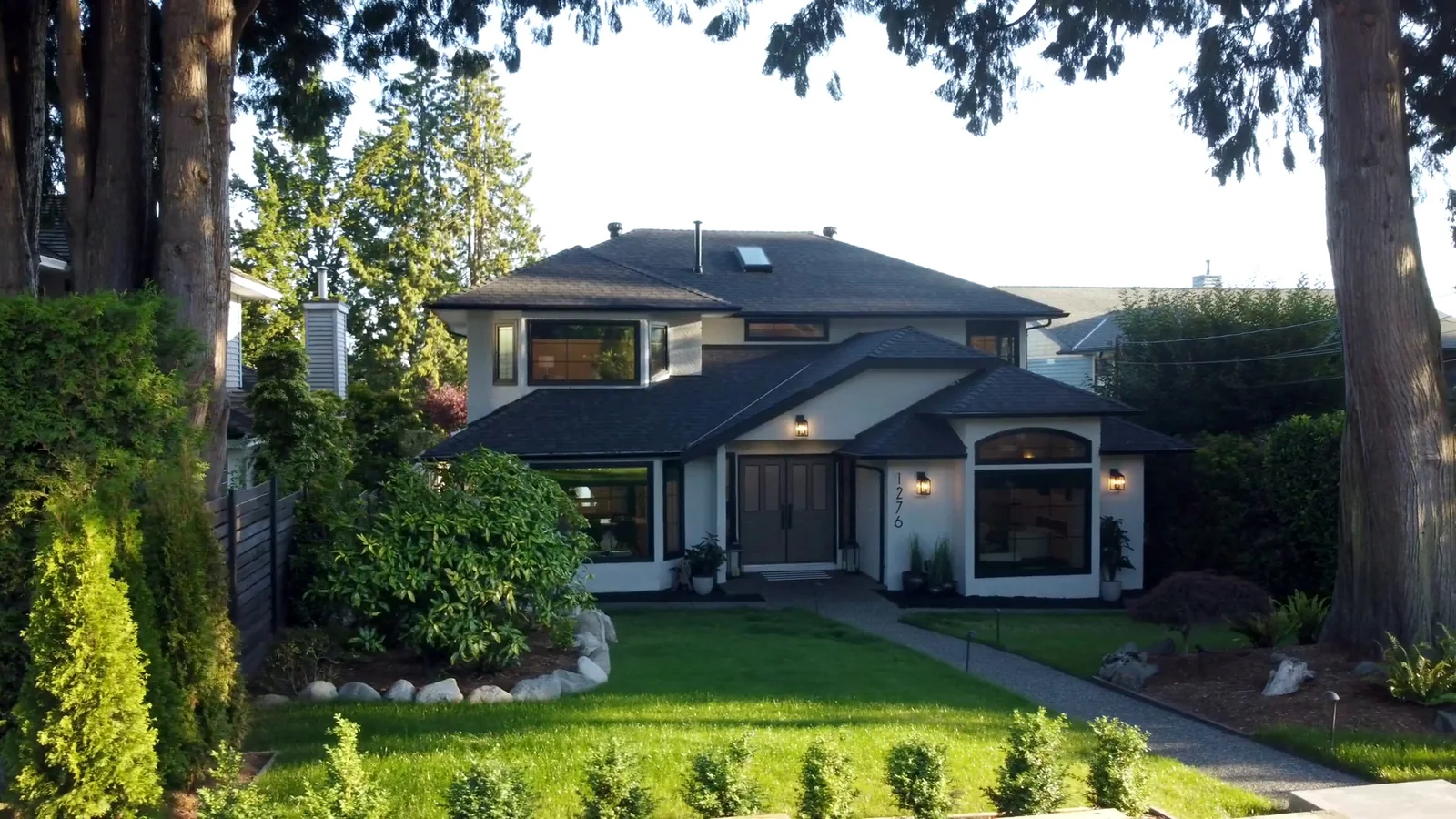 Remodelled West Vancouver home exterior with dark cedar siding, standing-seam metal roof, and mature landscaping — home renovation by DELANA Interiors