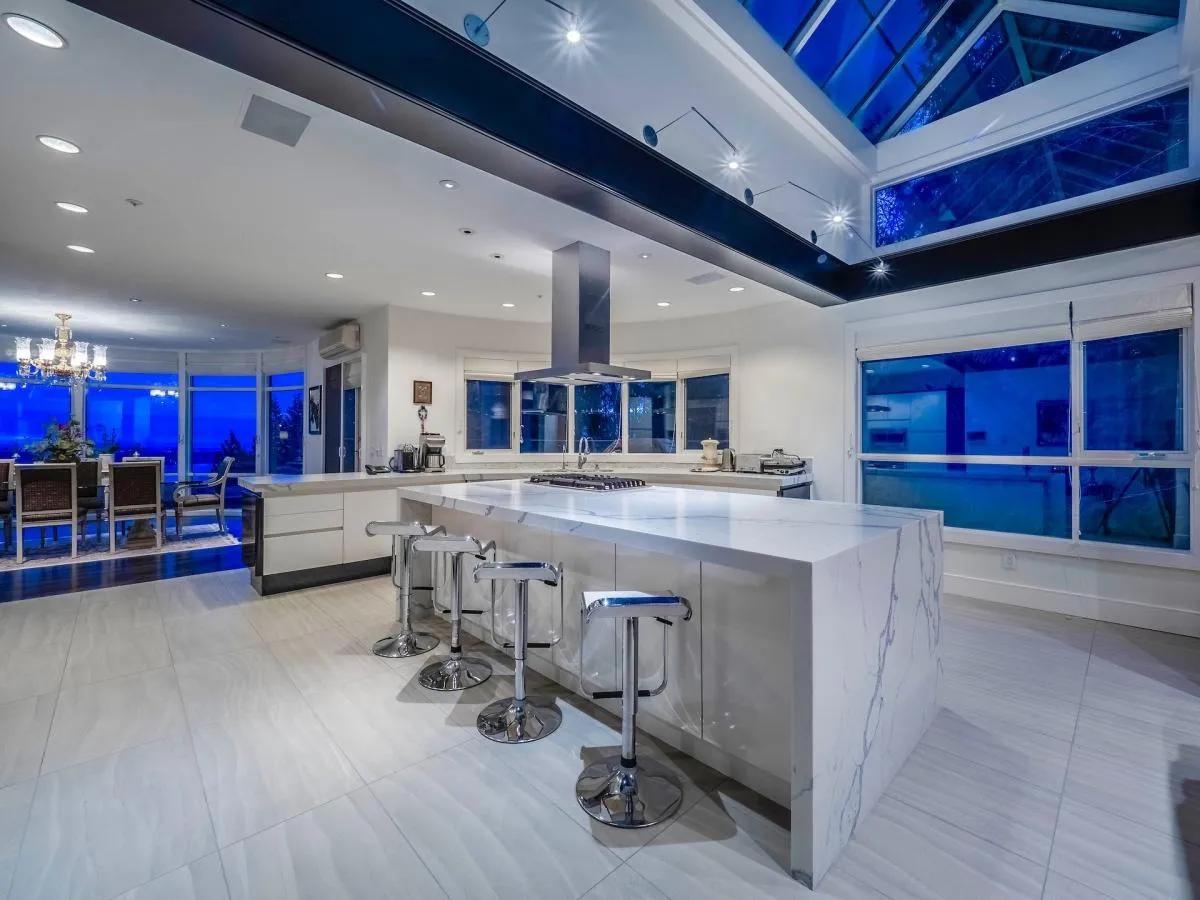 Renovated kitchen with Calacatta marble island, chrome bar stools and dramatic pyramid glass skylight at 1588 Pinecrest Drive, West Vancouver — DELANA Interiors