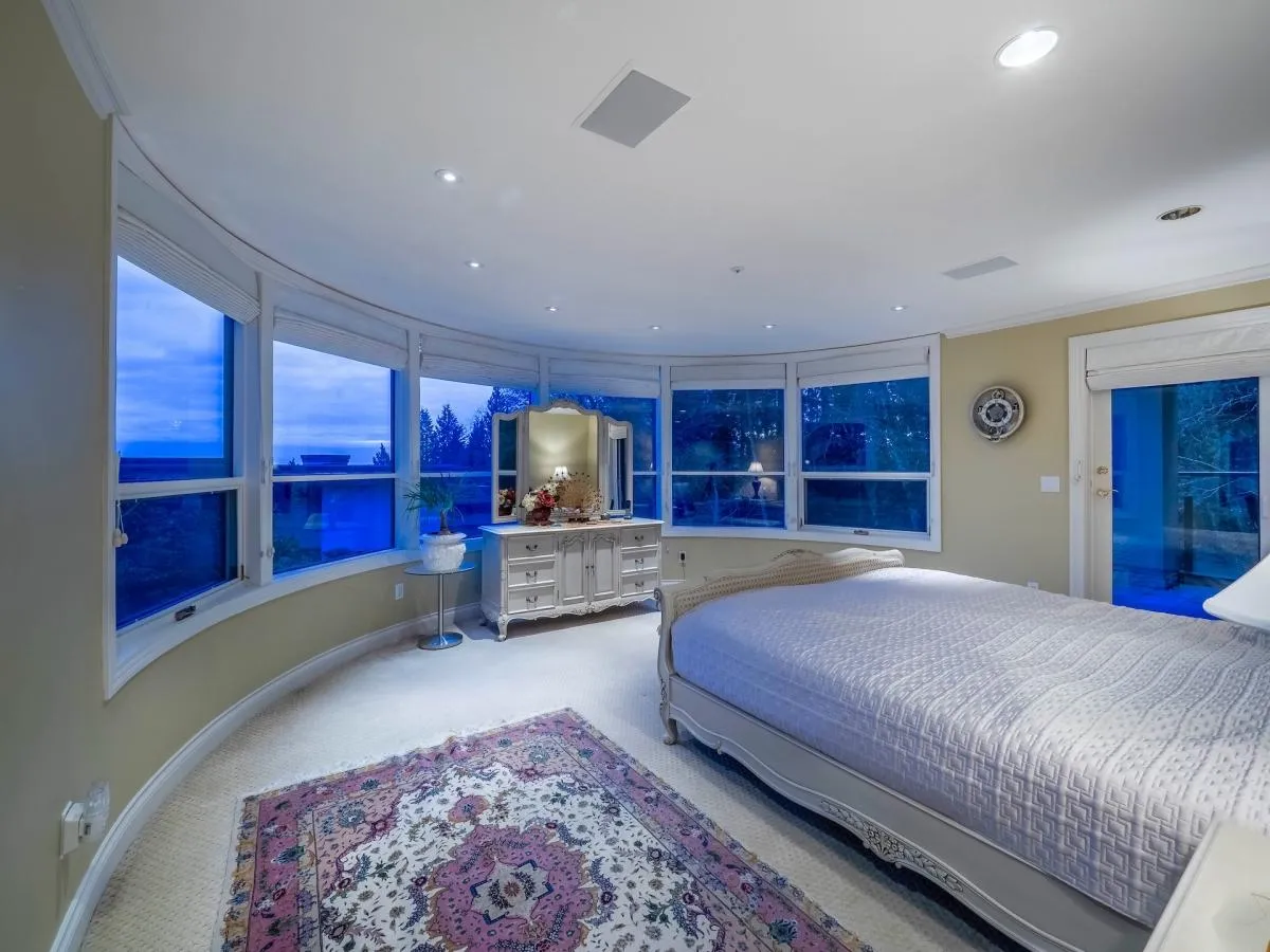 Renovated primary bedroom with curved panoramic window wall and ocean view at 1588 Pinecrest Drive, West Vancouver — DELANA Interiors