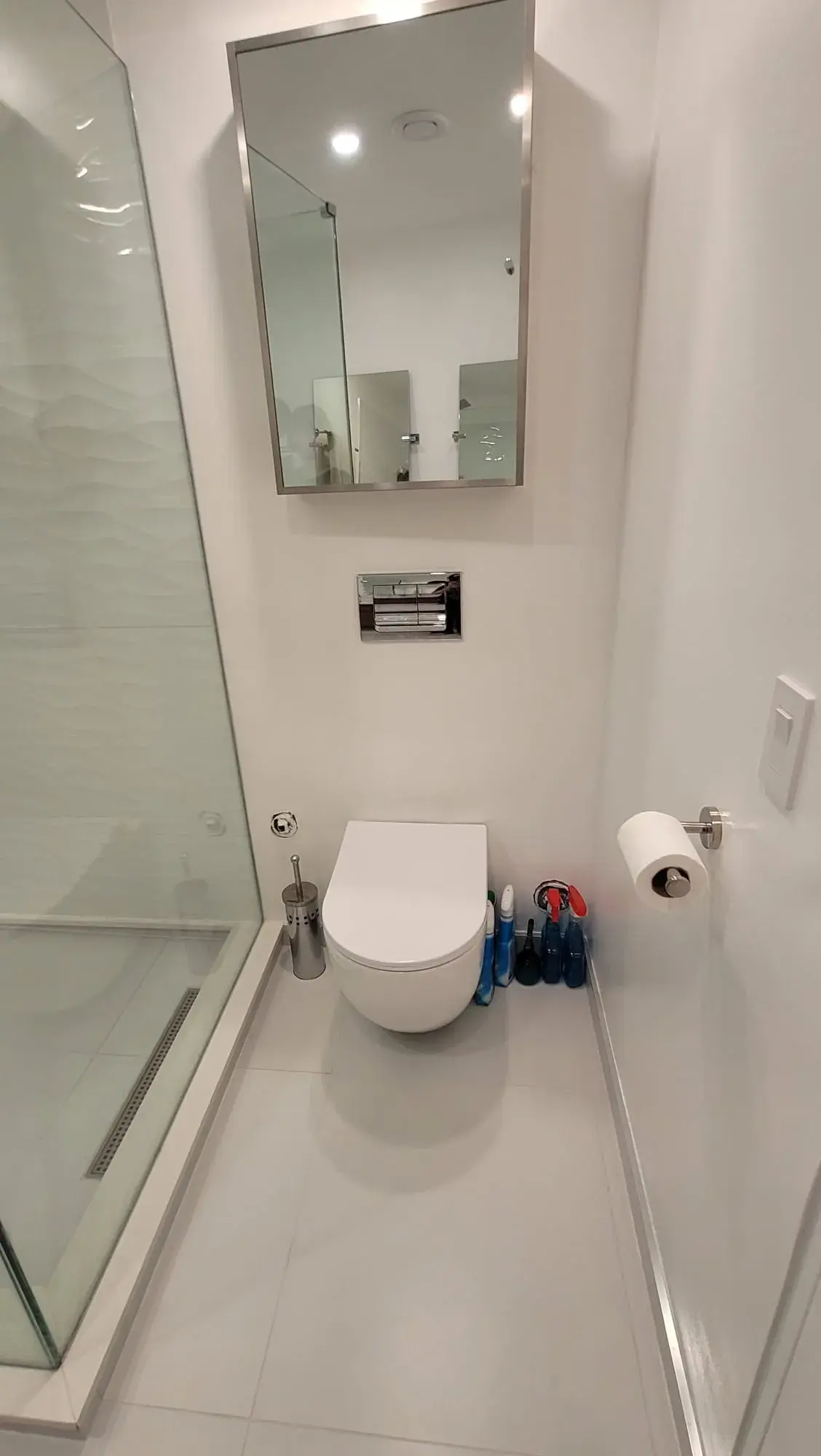 Minimalist white bathroom with wall-mounted toilet, recessed mirror cabinet and glass shower enclosure — bathroom renovation Vancouver