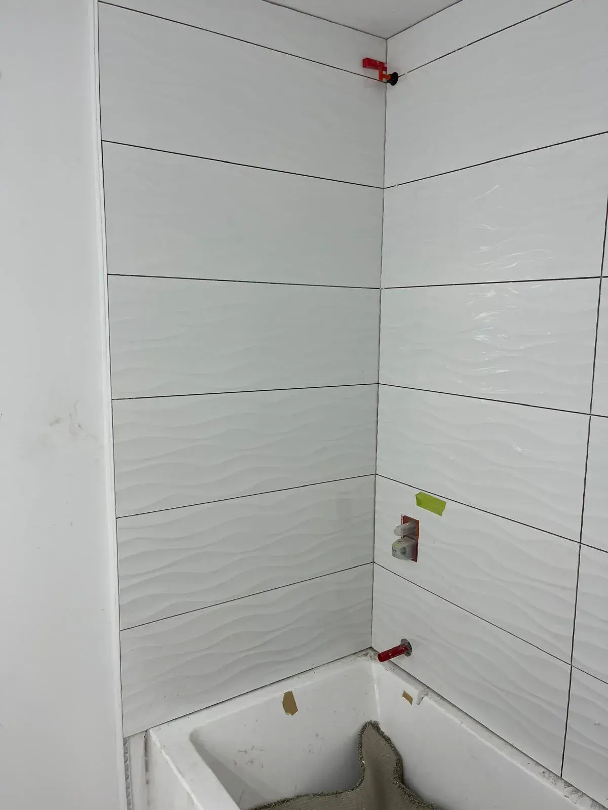 Precision installation of textured wave tile on bathroom shower surround with levelling clips — bathroom renovation Vancouver