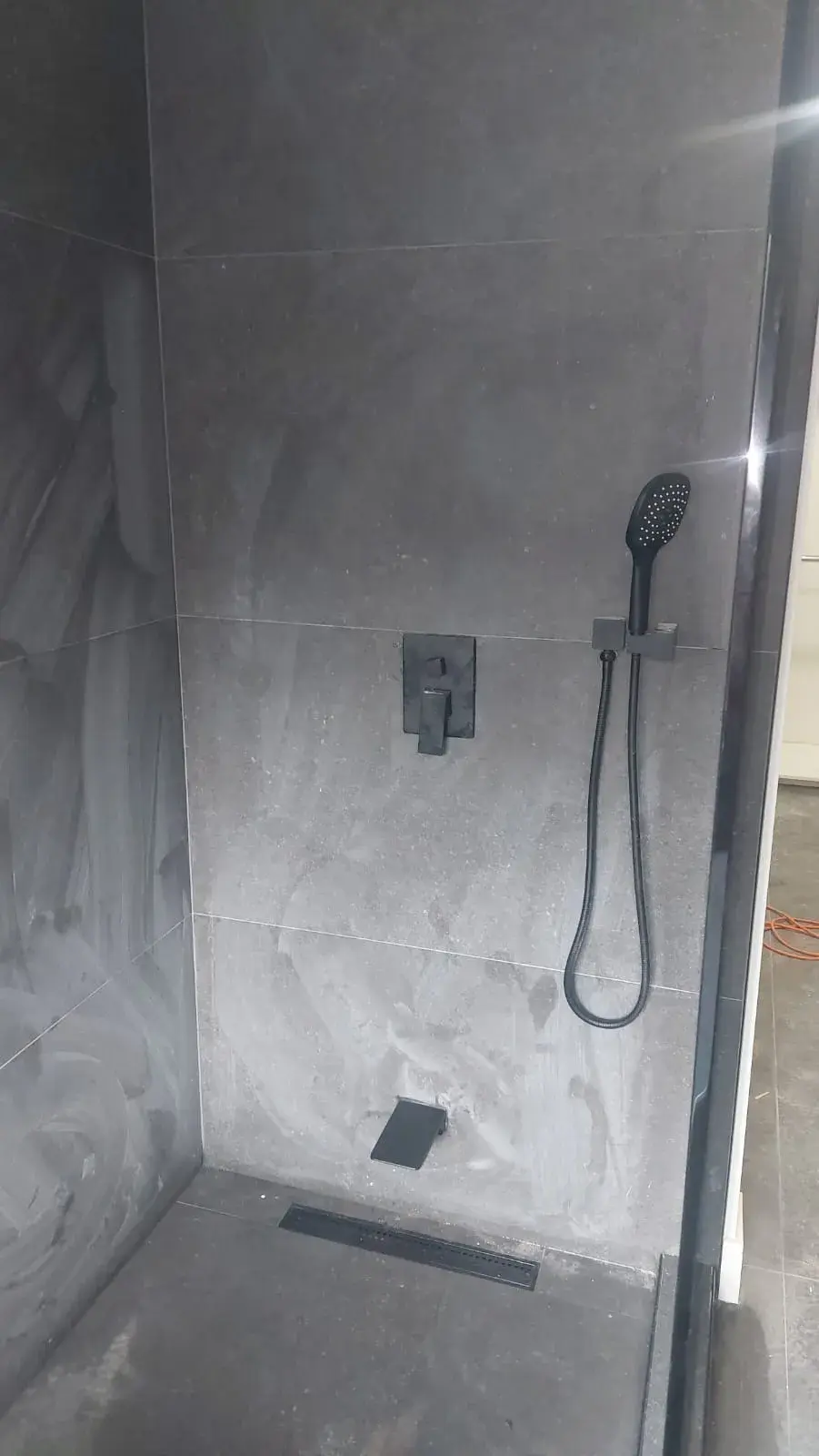 Dark charcoal walk-in shower with matte black handheld fixture and large format stone tile walls — bathroom renovation Vancouver